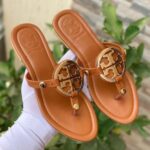 Tory Burch classic flat shoes in white, brown, and black with logo detail.