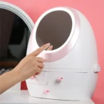 Rechargeable makeup mirror with a dimming LED light ring, sitting on a round cosmetic storage box base, showing its spin or rotating function for a portable vanity setup.