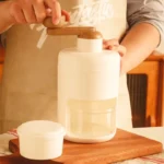 Manual hand-crank ice crusher machine with a visible collection mold/cup, showing its commercial-grade housing and mechanism for making crushed or shaved ice.