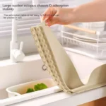 Flexible silicone sink baffle plate/splash guard in a kitchen sink, shown attached to the edge to prevent water and oil from spraying onto the counter.