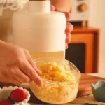 Manual hand-crank ice crusher machine with a visible collection mold/cup, showing its commercial-grade housing and mechanism for making crushed or shaved ice.