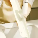 Flexible silicone sink baffle plate/splash guard in a kitchen sink, shown attached to the edge to prevent water and oil from spraying onto the counter.